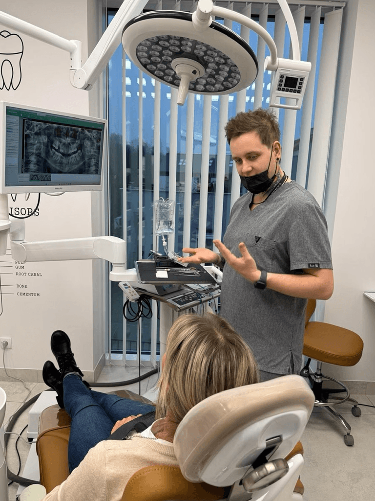 Chirurg stomatolog tłumaczący proces wszczepienia implantu zęba pacjentce przy zdjęciu rentgenowskim w gabinecie stomatologicznym