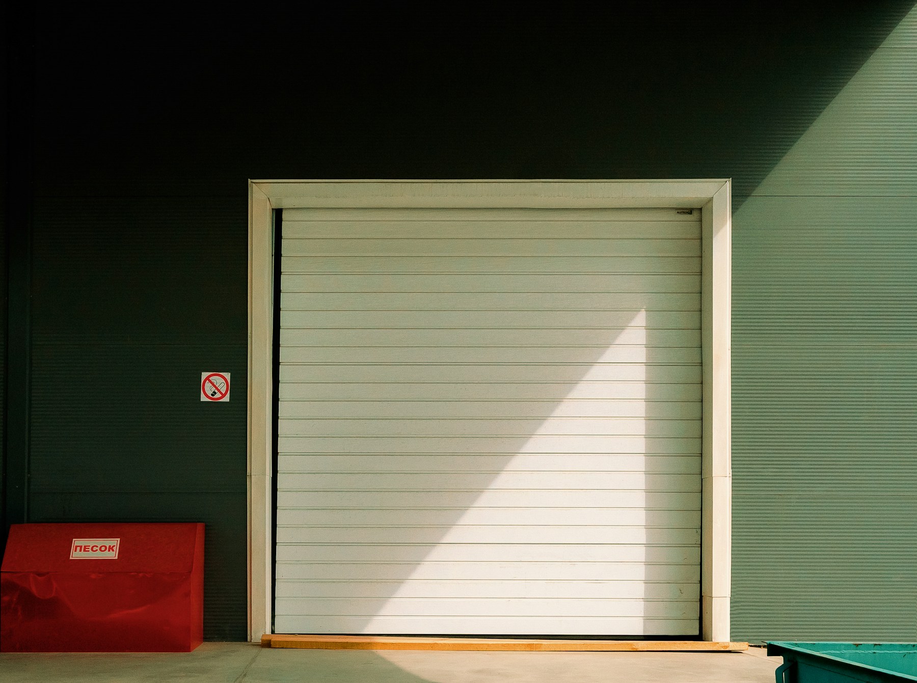A white roller door in a green workshop wall