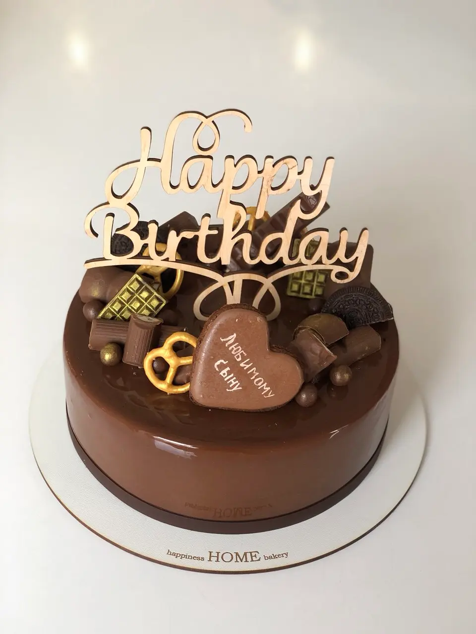 Chocolate cake with wooden "Happy Birthday" topper and chocolate decorations including heart and pretzel