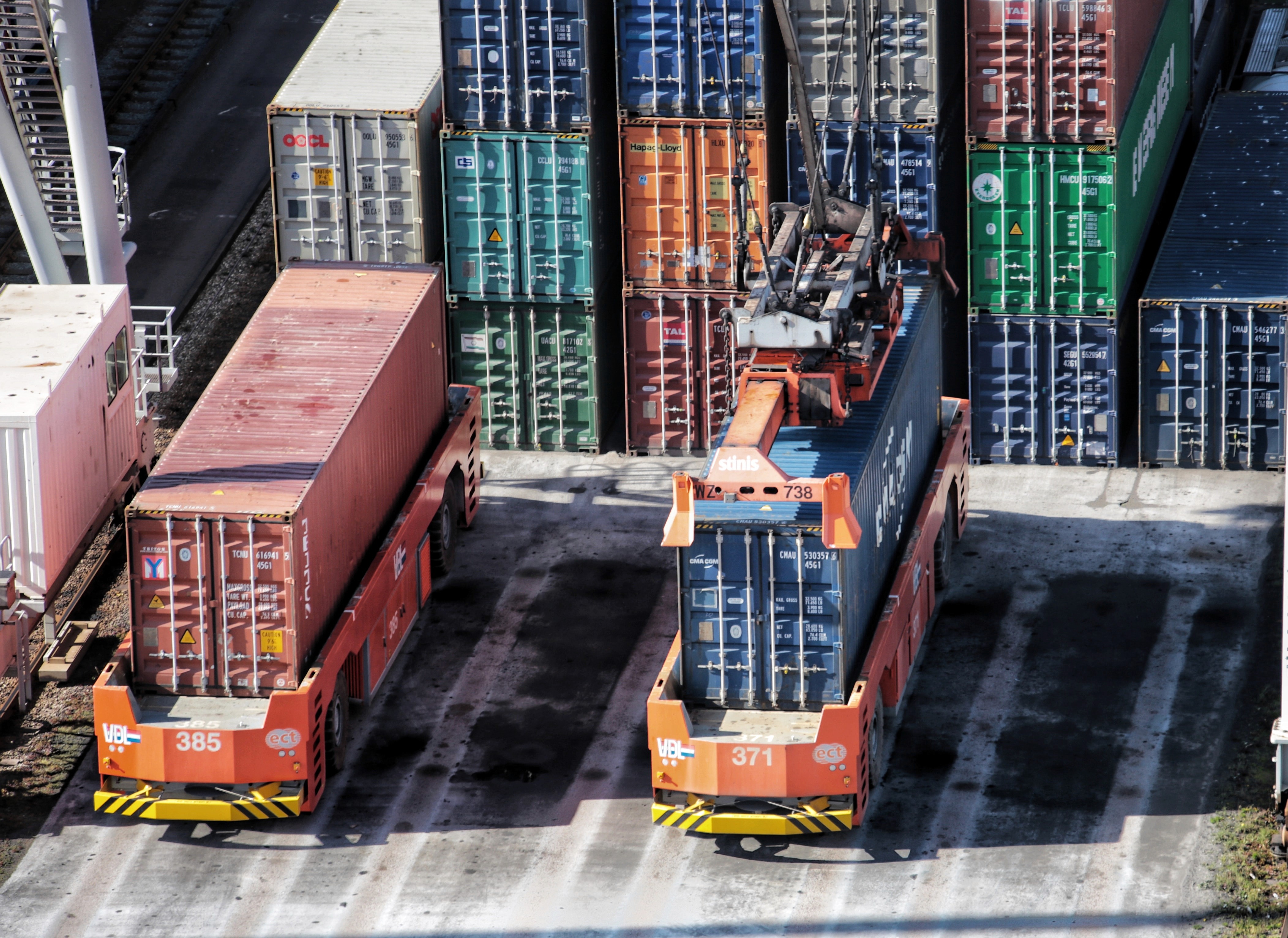 photo of a port's logistics yard with a series of containers of different colors, stacked and a crane positioning one of the containers on an automatic truck without a cabin