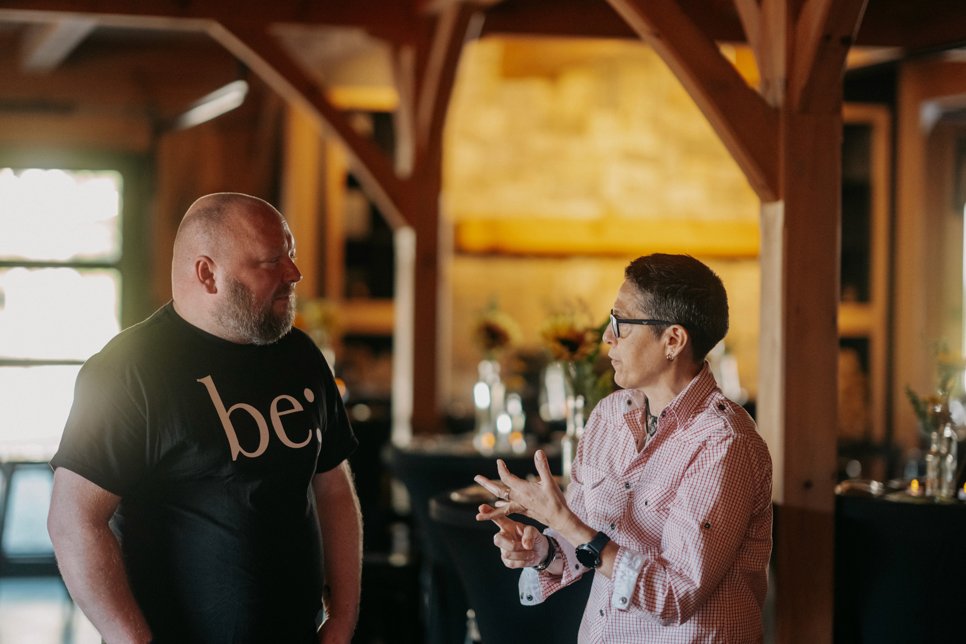 Two attendees in conversation at a be; community event, connecting in a warm, inclusive gathering space in Bridgewater, Massachusetts
