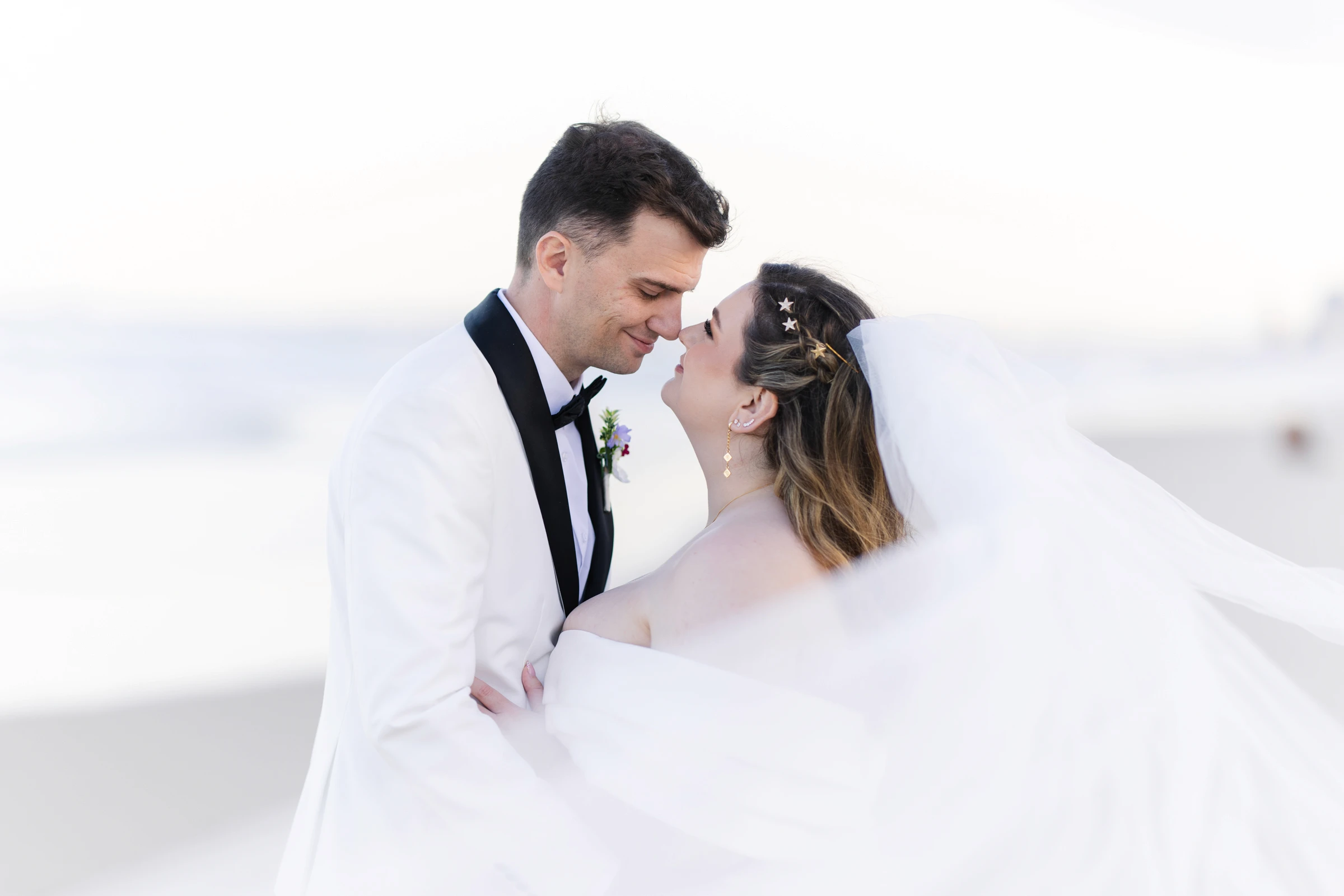 Bride and groom touching noses at the beach