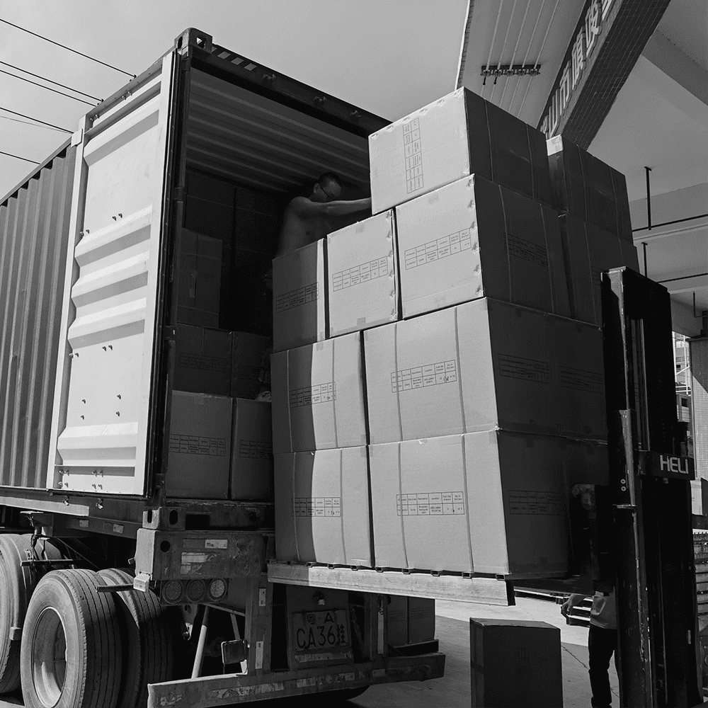 Black and white shot of a logistics worker and forklift loading large cardboard shipping crates into a freight container for international furniture export.