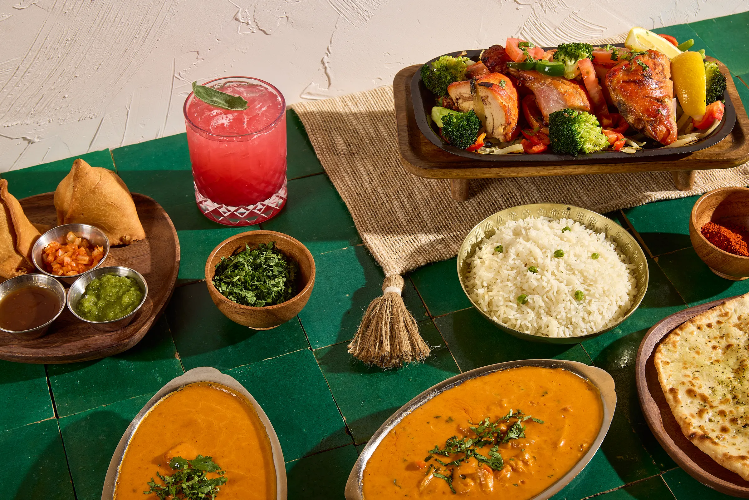 Curries, rice, samosas and grilled chicken on a green tile table