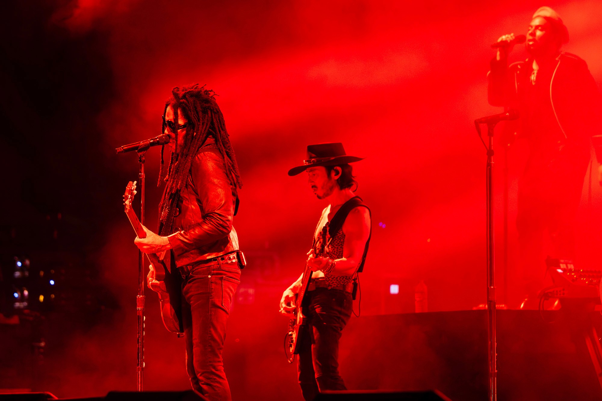 Trois musiciens sur scène dans une lumière rouge intense, guitaristes et chanteur