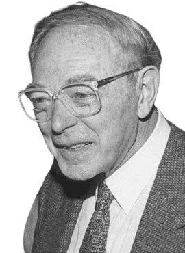 A black-and-white portrait of an elderly man wearing large glasses, a suit jacket, and a patterned tie, smiling warmly. The image captures a scholarly and friendly demeanor, with a close-up focus on his face, highlighting the details of his expression and his classic, professional attire.