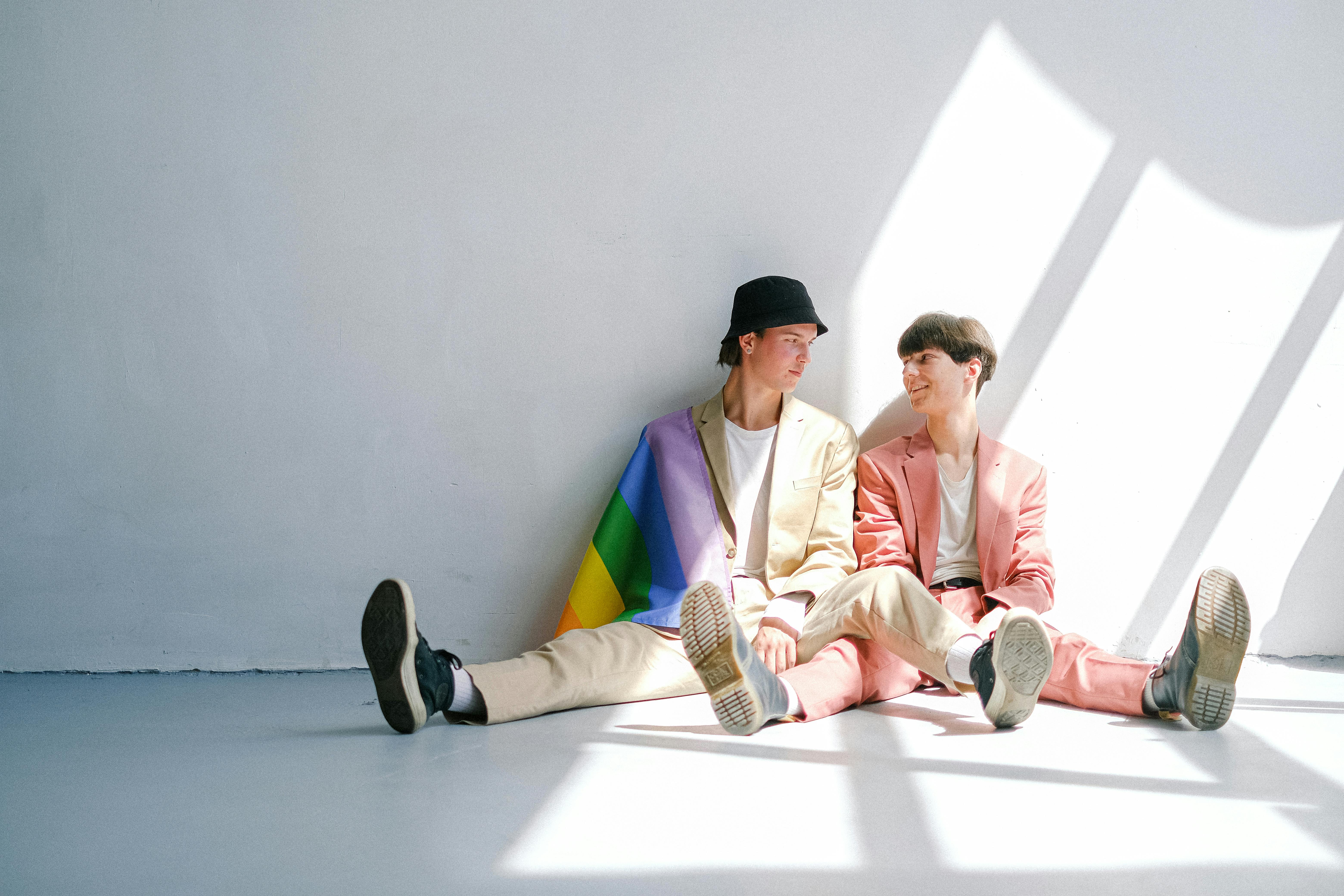 Two people sitting in an empty room with rainbow flag