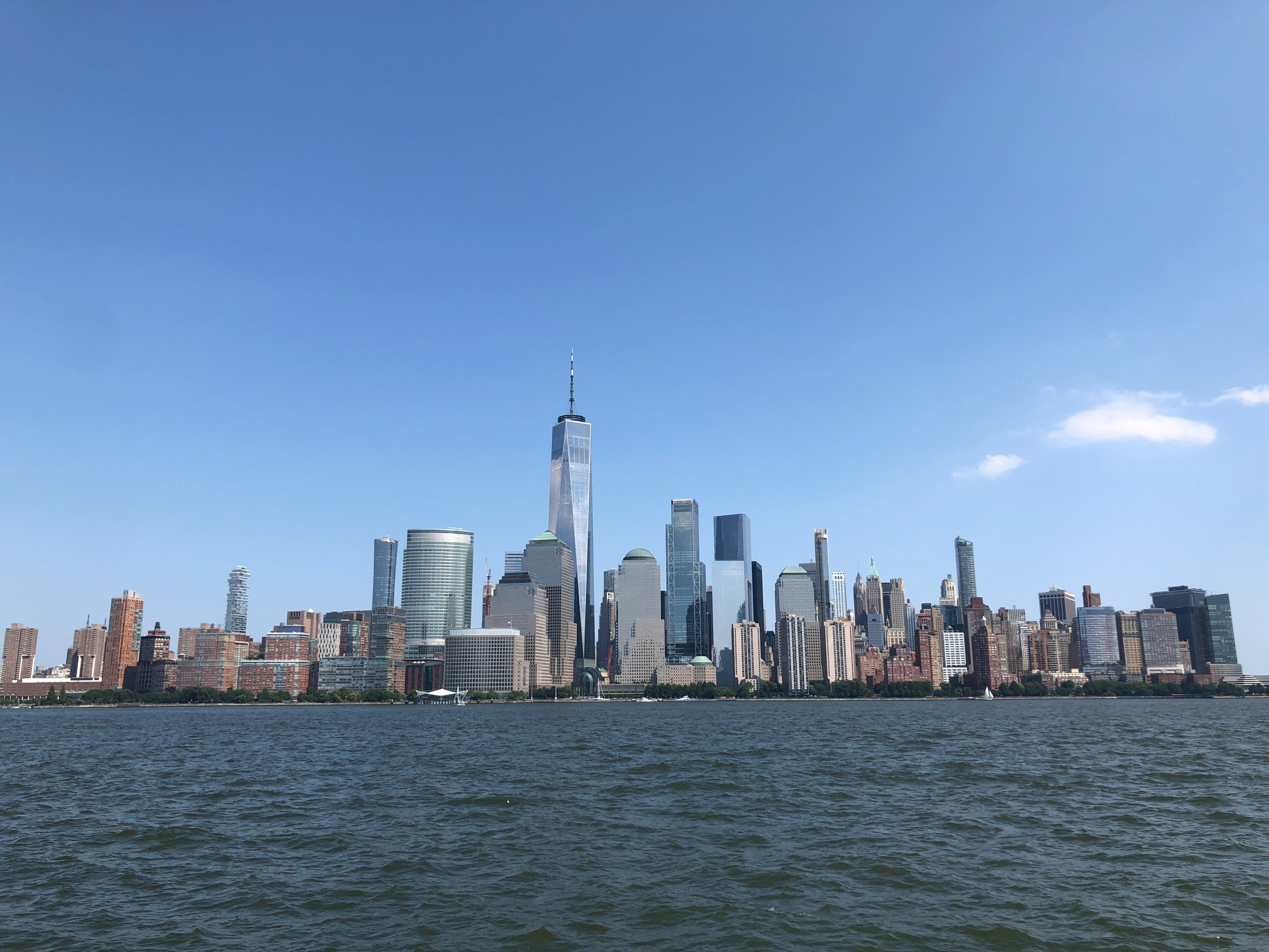 City skyline on a clear day, featuring tall buildings and a distinctive tower, viewed from the water.