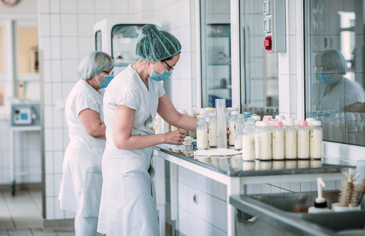 Egészségügyi dolgozók anyatejet vizsgálnak és palackoznak higiénikus laborban, maszkban.