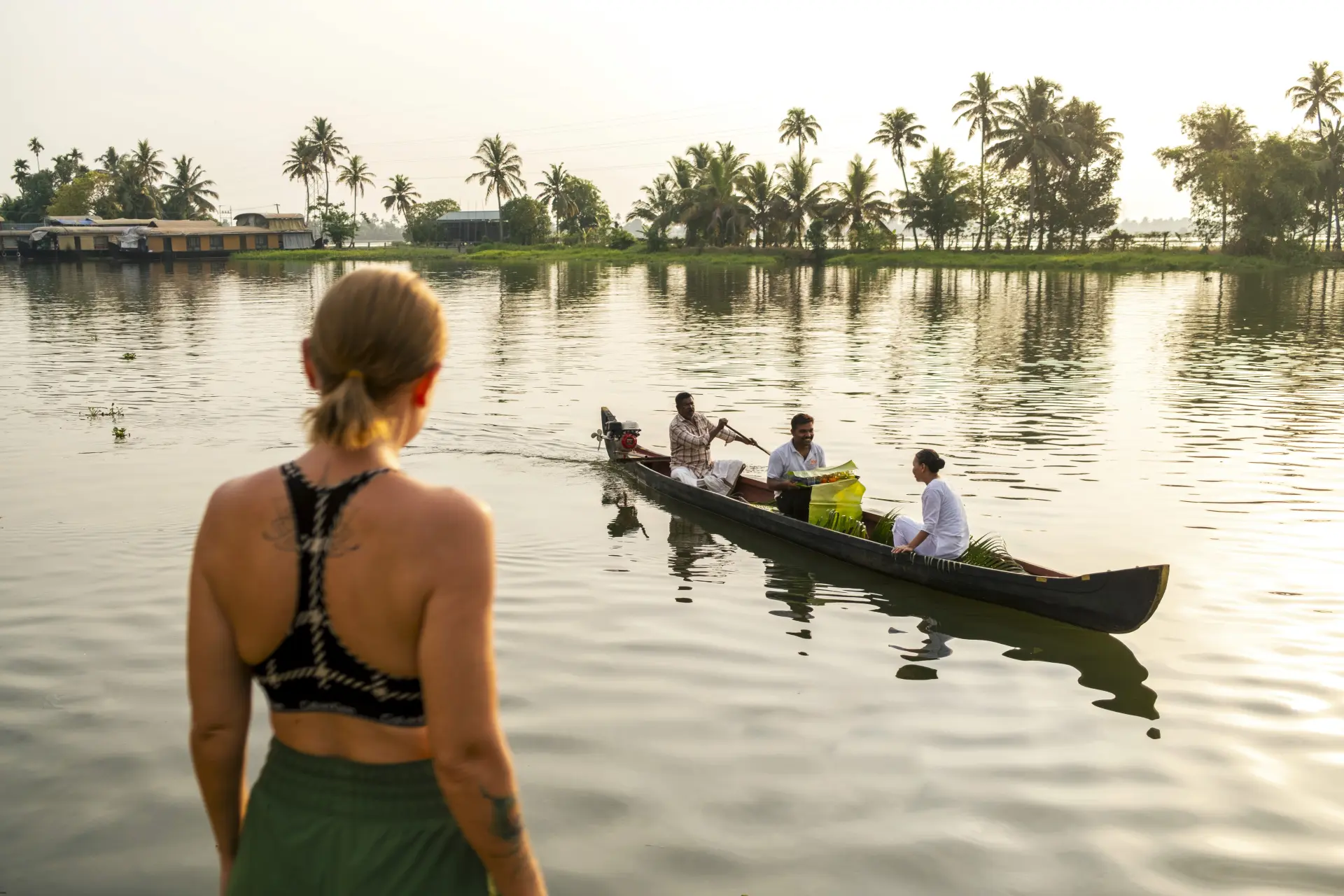 Guest watching a traditional canoe glide across the Alleppey backwaters at sunrise, part of the Vedic Village wellness experience