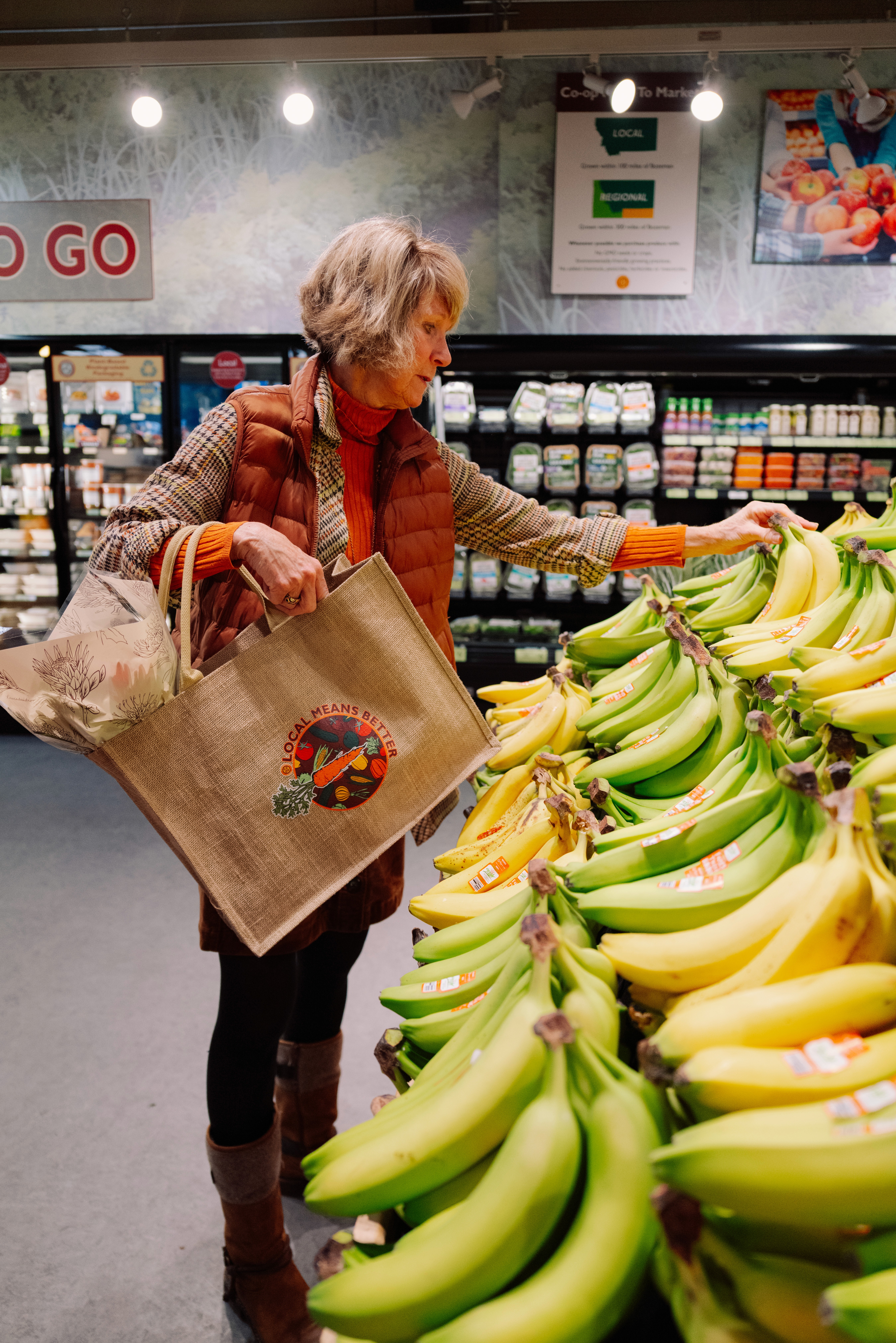 A reusable grocery bag surrounded by various fresh vegetables and fruits on a wooden surface.