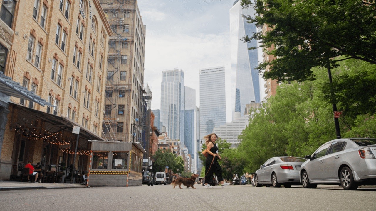 Urban street scene with tall buildings, trees, and people walking on the sidewalk