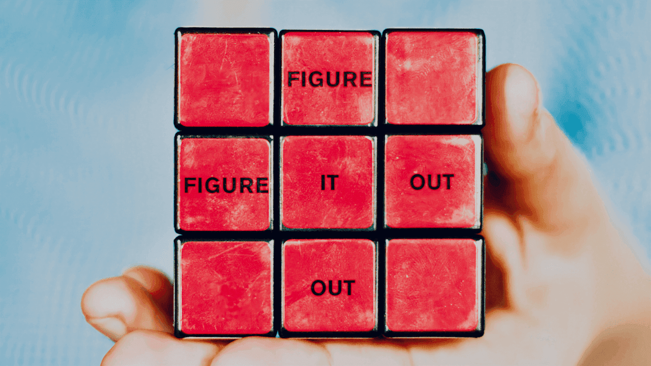 A hand holds a Rubik’s cube with the phrase “FIGURE IT OUT” on its side.