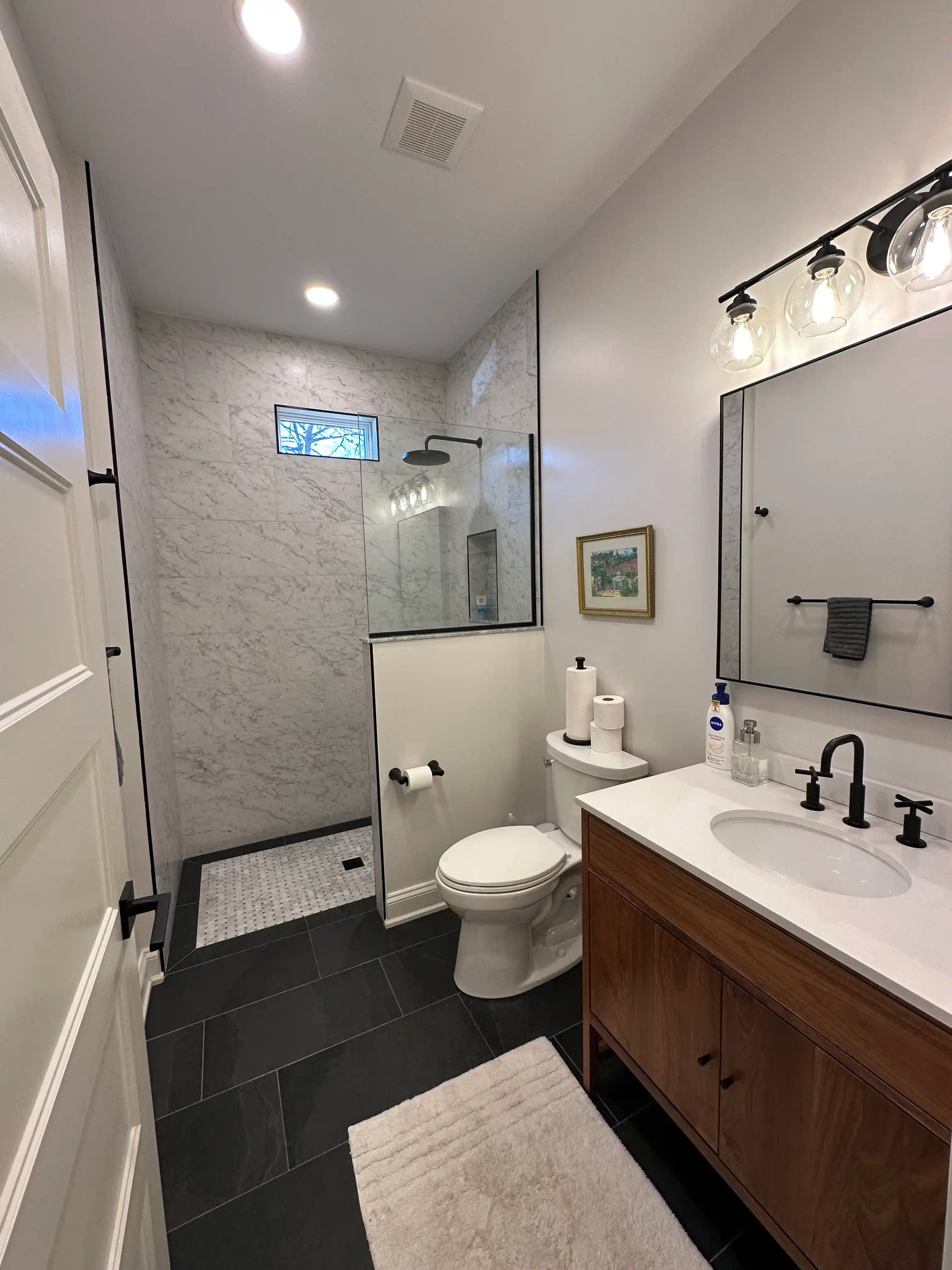 Remodeled bathroom with glass-enclosed tiled shower, white vanity, modern fixtures, recessed lighting, and efficient layout.