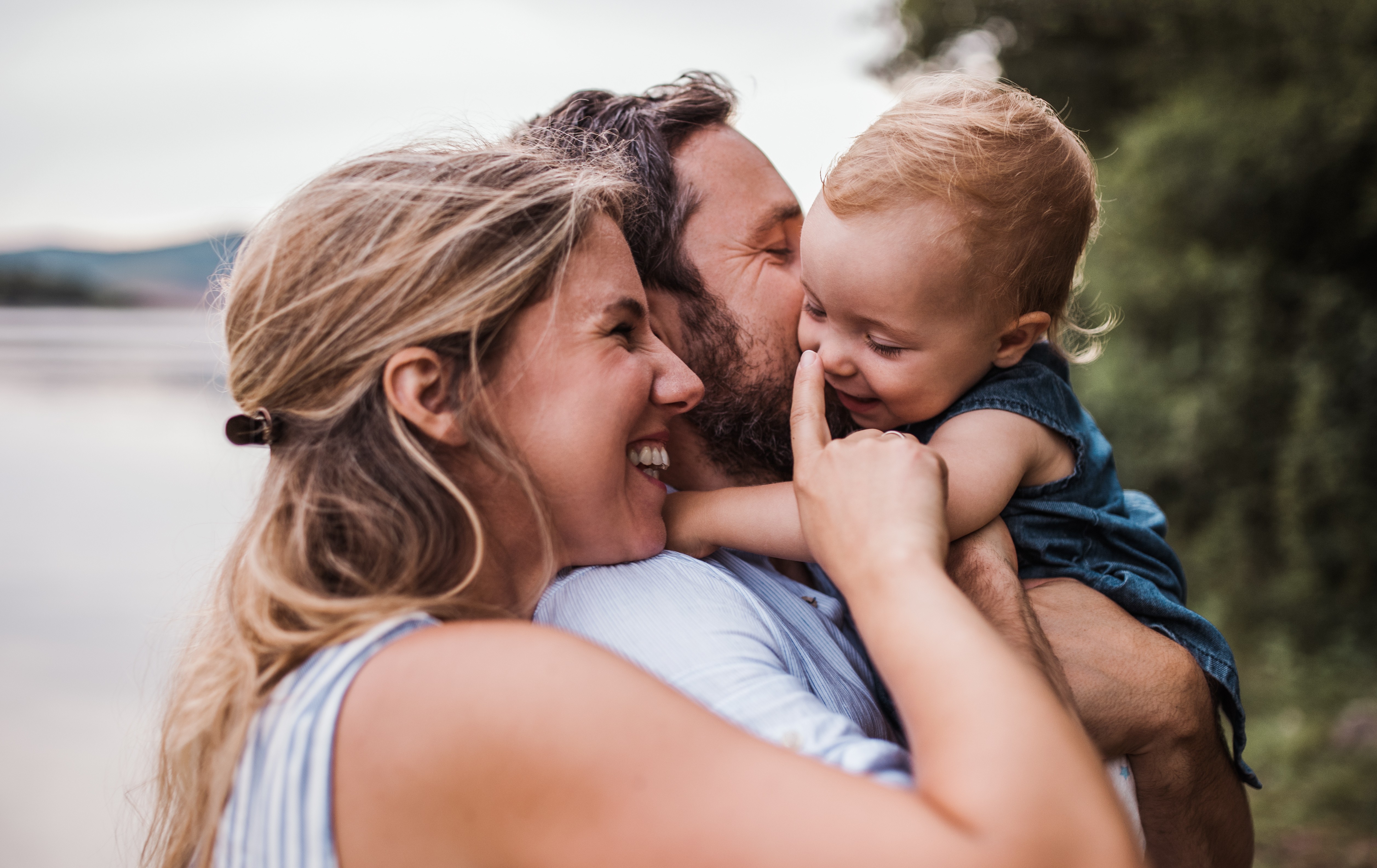 miling parents hugging their baby outdoors