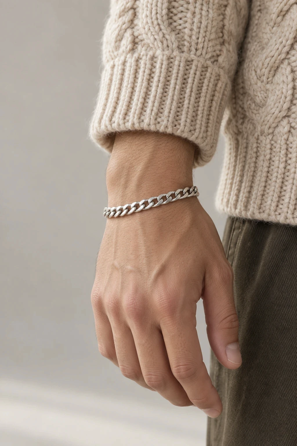 Silver curb chain bracelet on a wrist beside a cable knit cuff