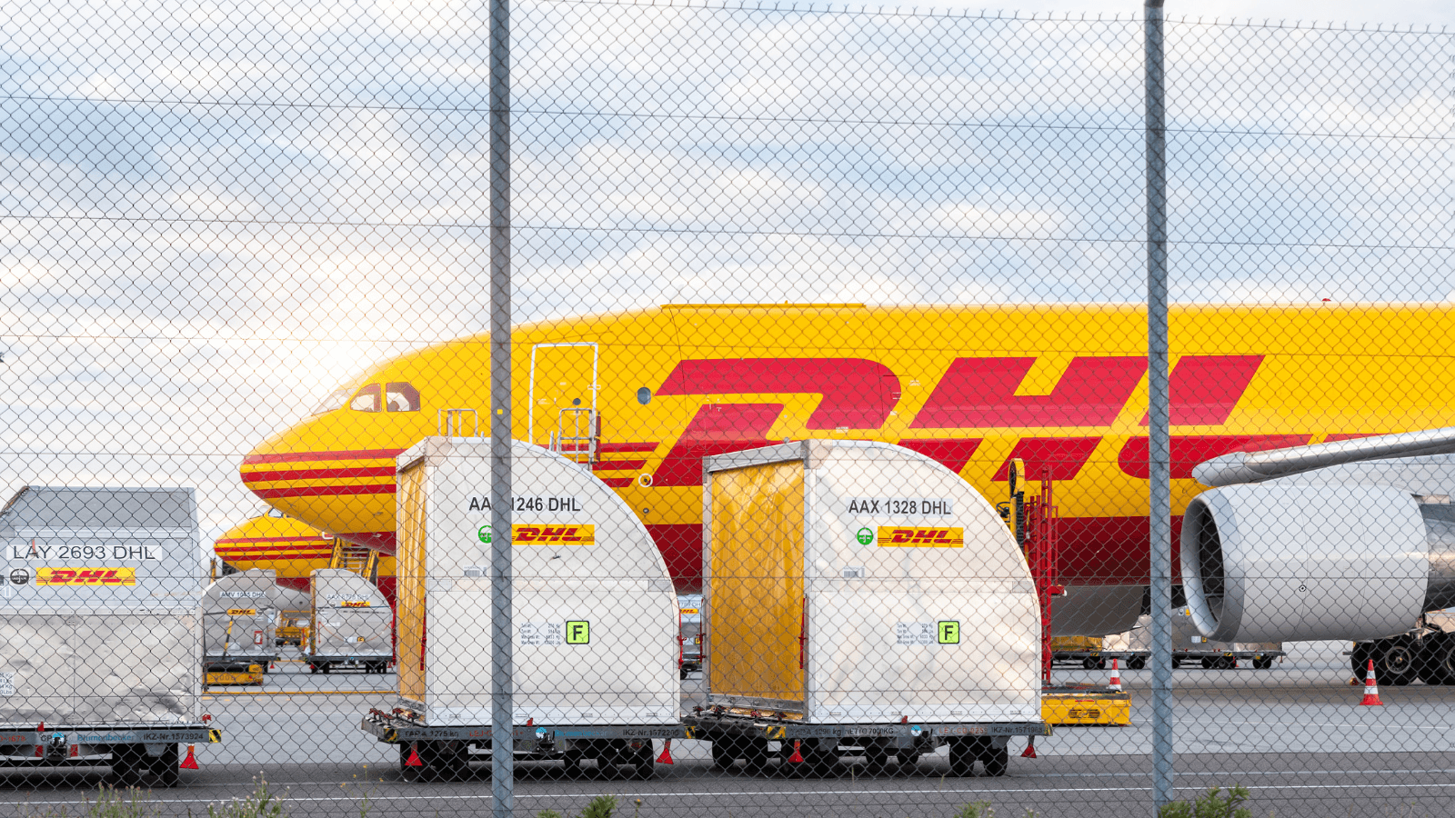 A DHL cargo plane at an airport with containers ready for loading, showcasing logistics industry news about DHL's expanded reverse logistics operations in 2025