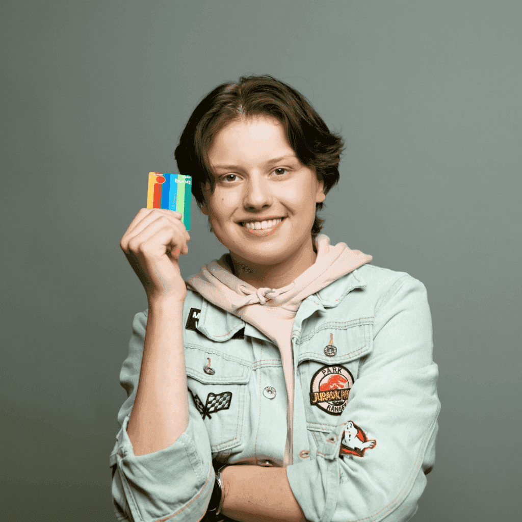 Persoon glimlacht en houdt kleurrijke objecten in hun hand, draagt een lichtgekleurde jas, tegen een neutrale achtergrond.