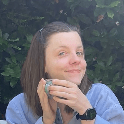 Portrait of Elsa holding a cup of coffee in front of a leafy background