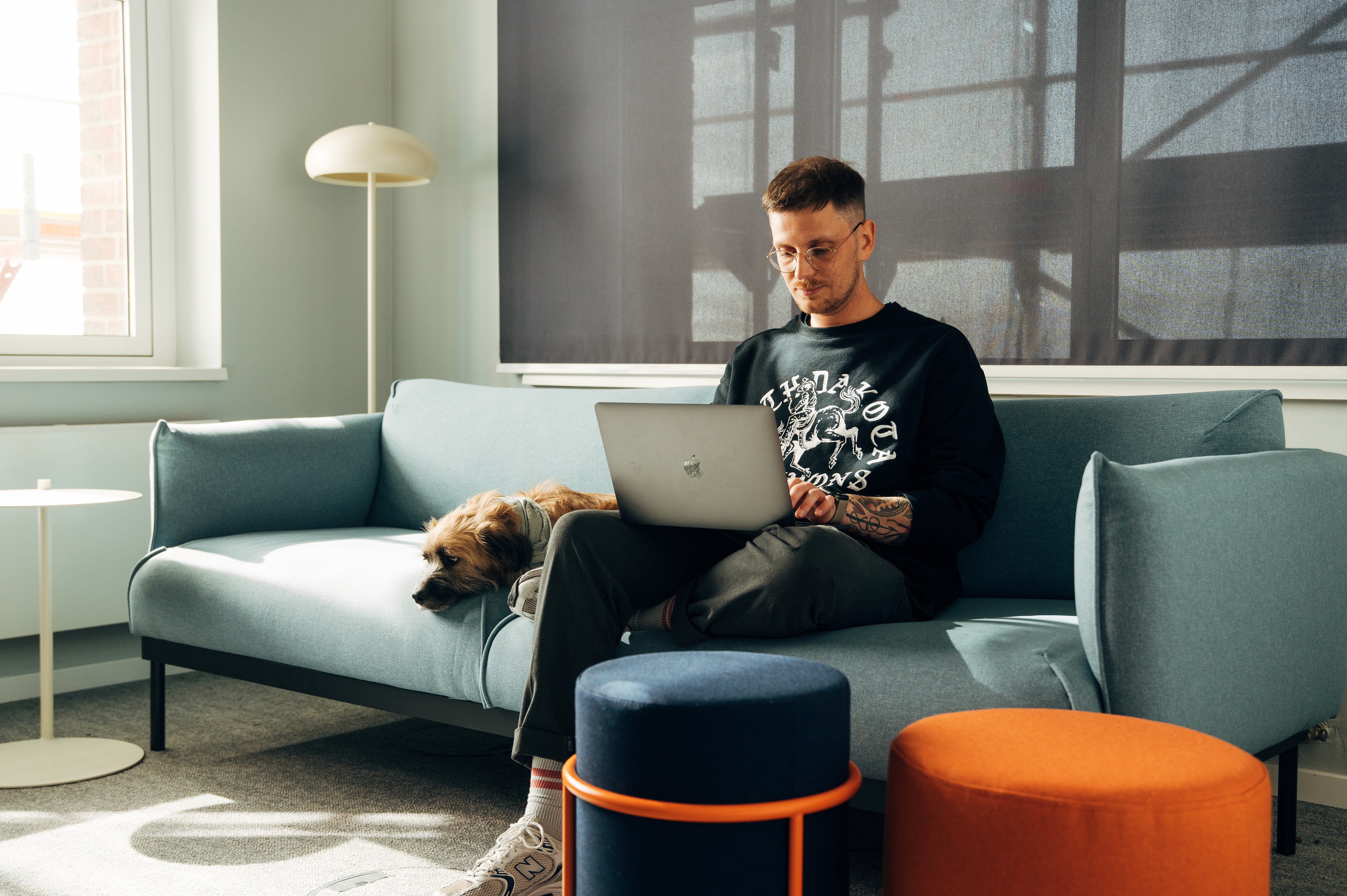 A person sits on a couch, using a laptop with a cozy living room setting in the background.