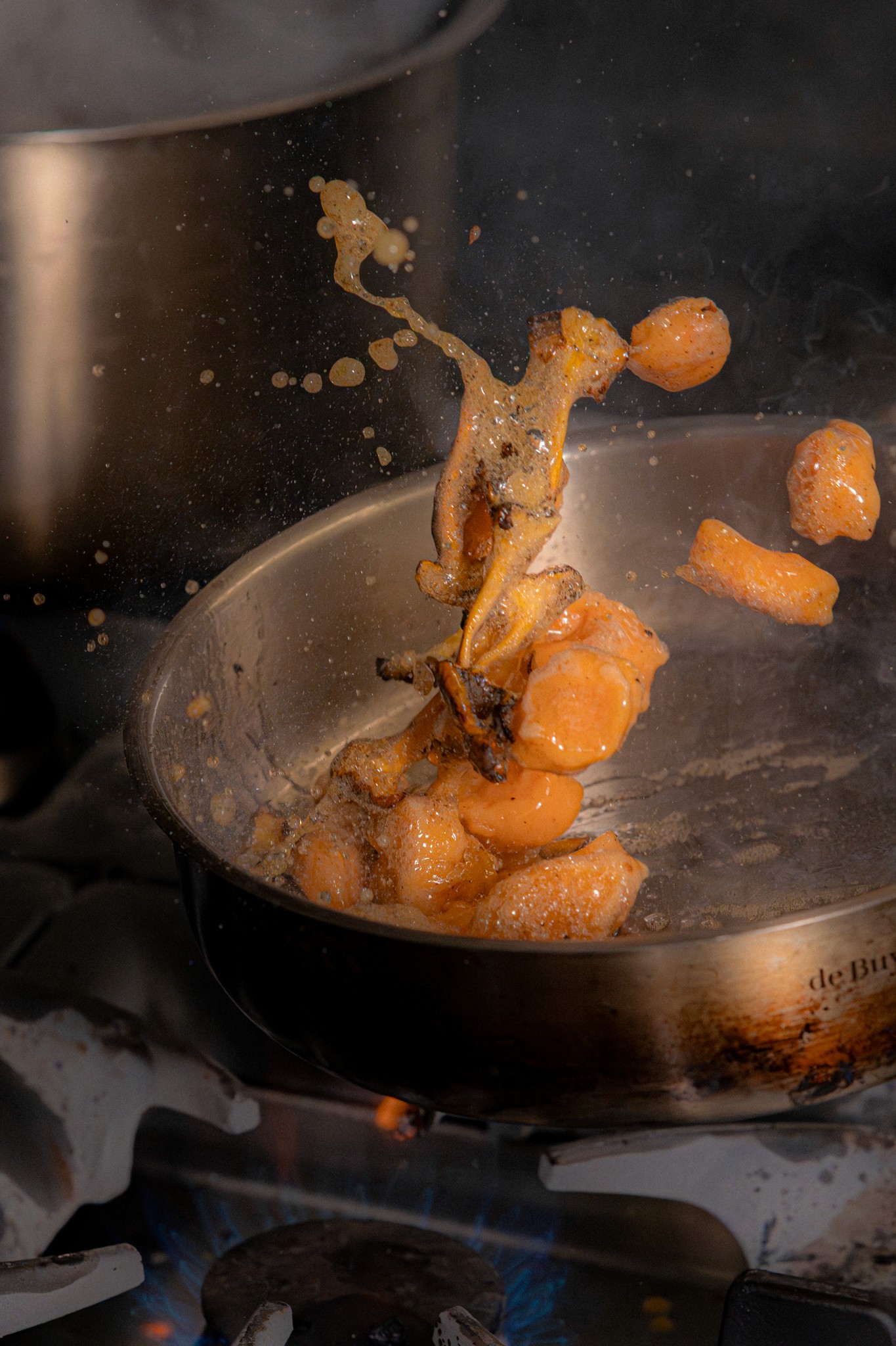 Poêlée en pleine action avec des ingrédients sautés, montrant l’énergie, la précision et le savoir-faire de la cuisine du restaurant.
