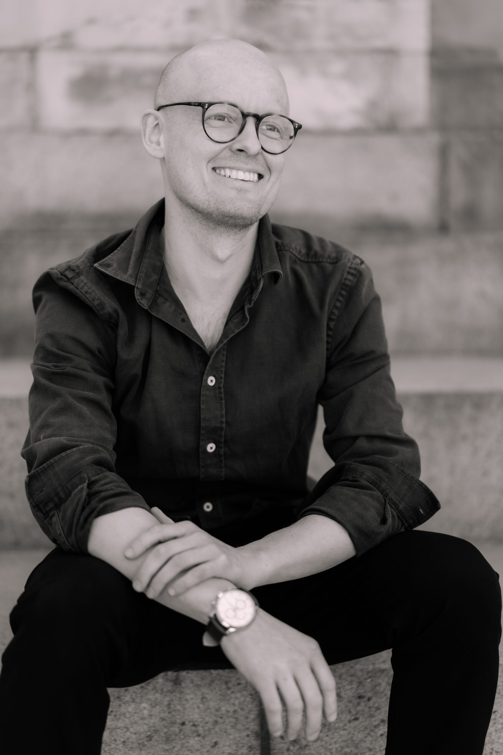 A woman with shoulder-length brown hair and freckles smiles softly. She wears a beige blazer over a white shirt in a warmly lit room, conveying professionalism and warmth.