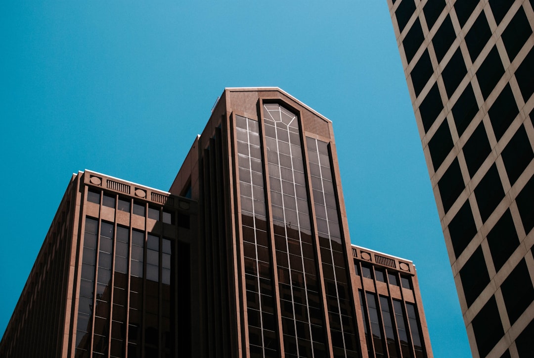 Upward view of two brown glass office towers against a clear blue sky.