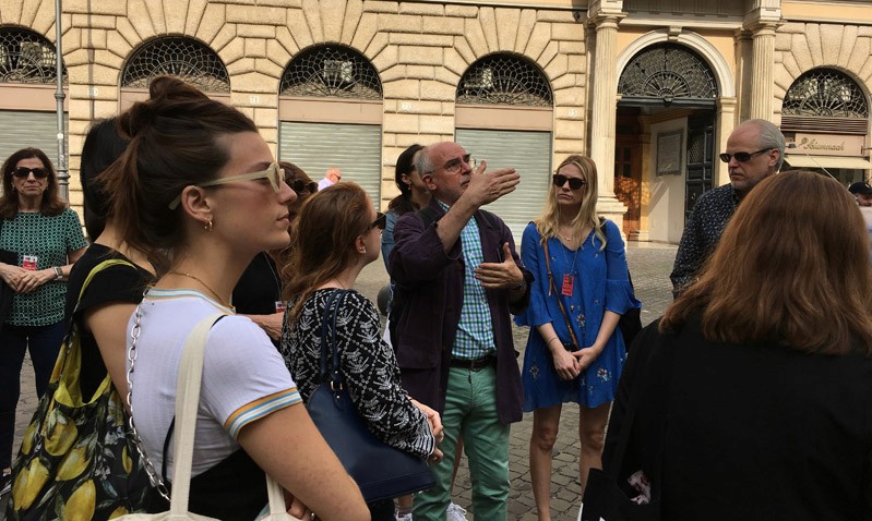 A photo of a group of students taking a tour and listening to a lecture while looking at some building architecture.