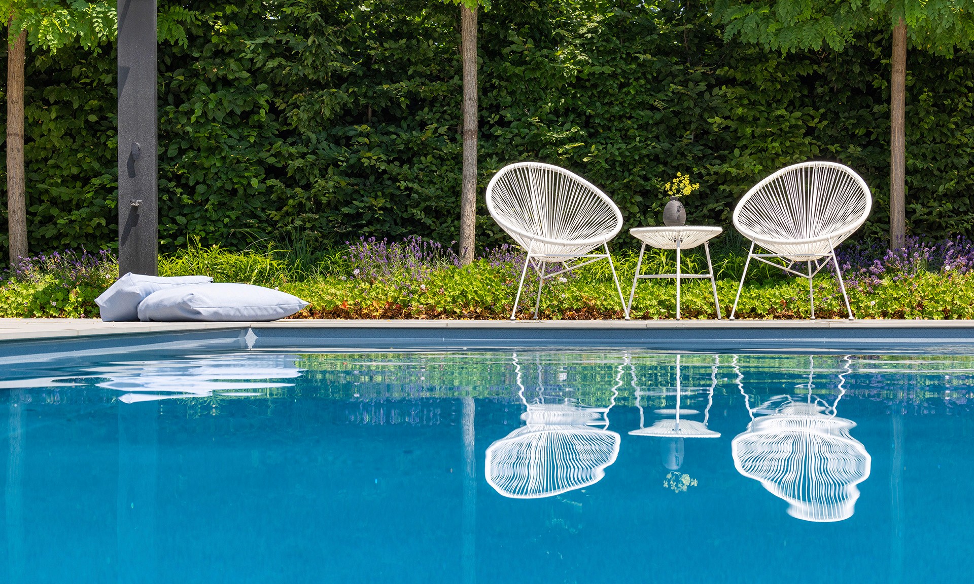 Poolbereich mit zwei Sesseln und kleinem Tisch vor dicht bepflanztem Gartenrand.
