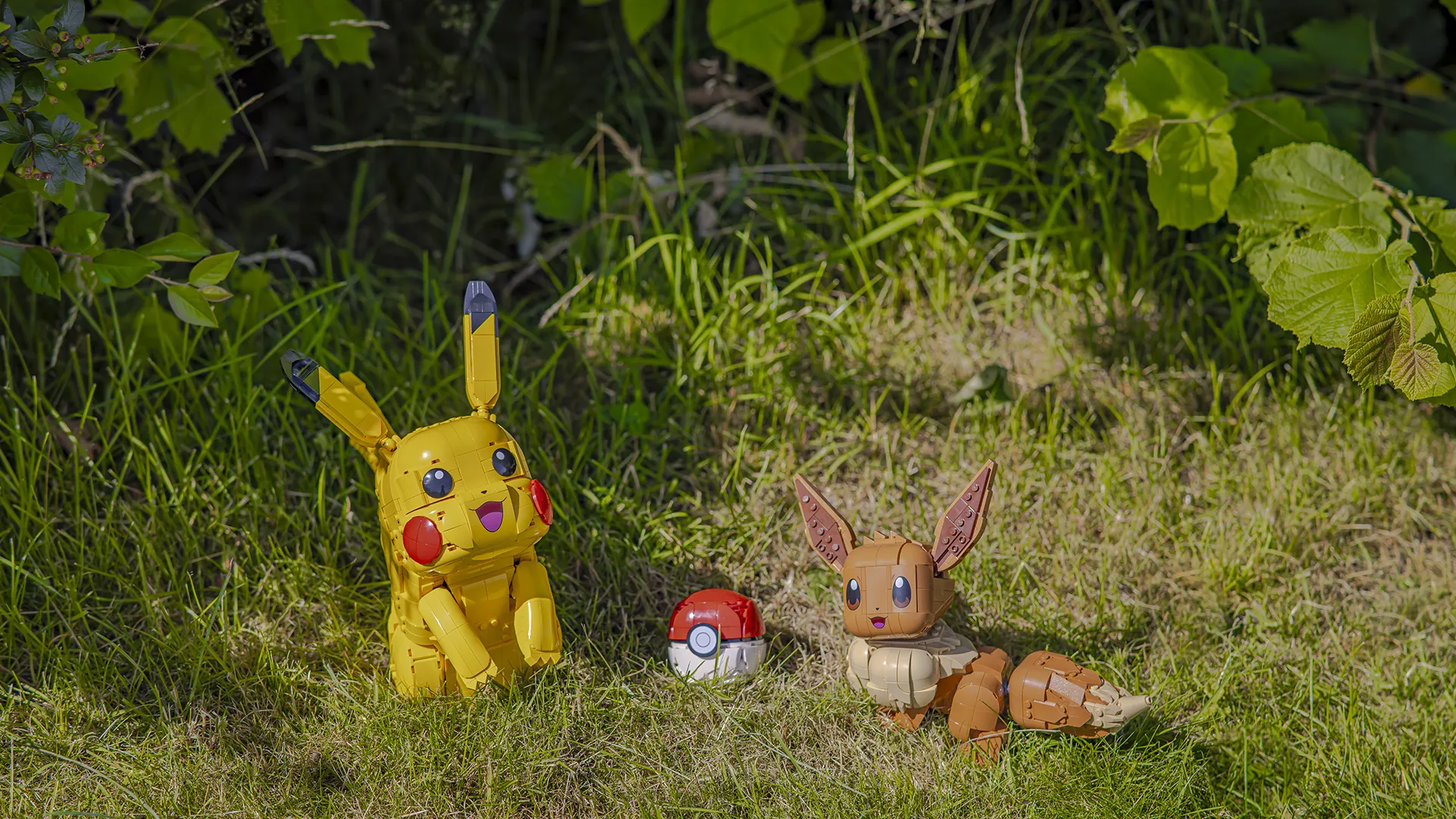 LEGO modell av Pikachu og Eevee sammen med en Pokéball utstilt utendørs i gresset