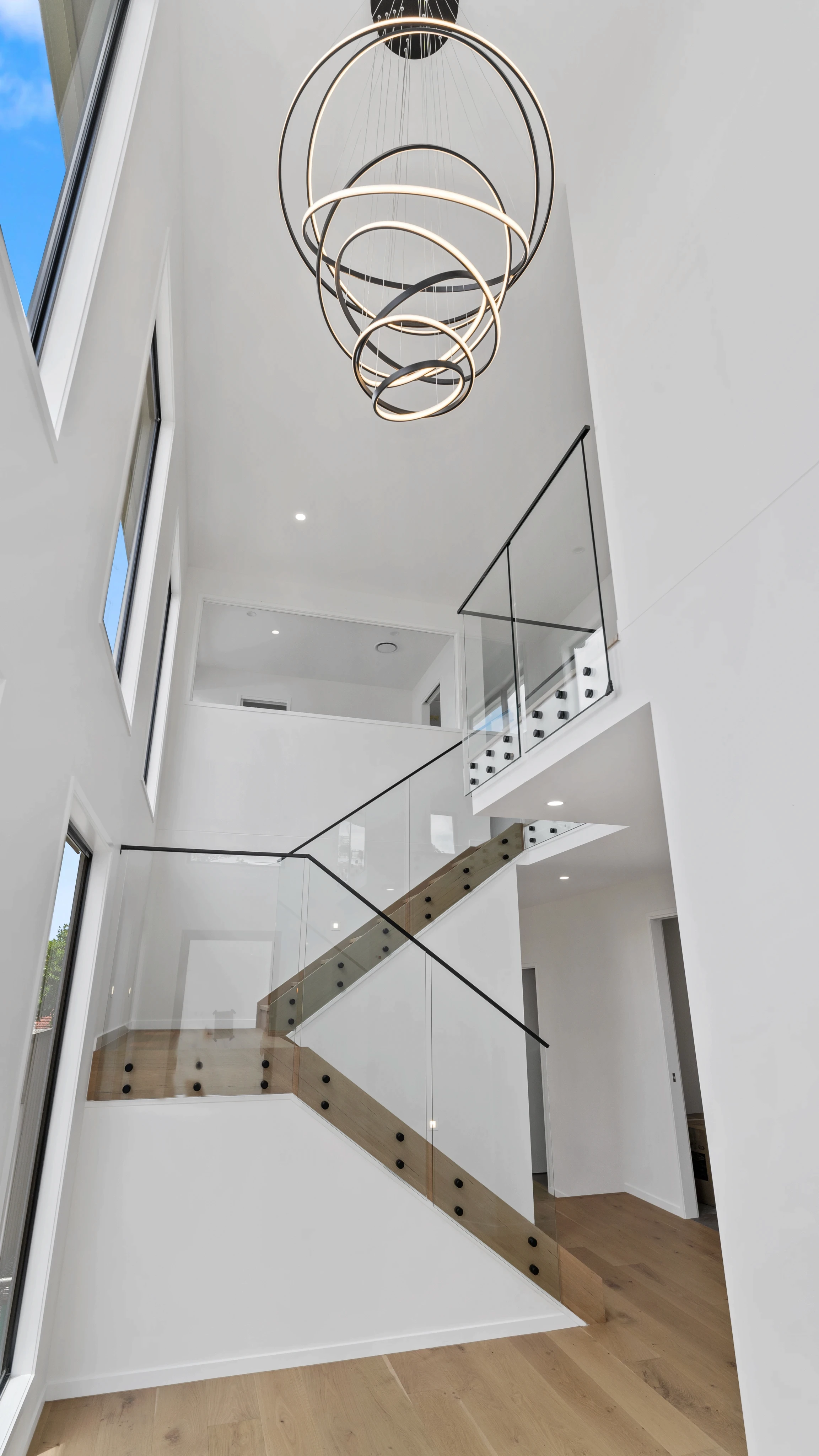 Open-tread staircase with glass balustrades in a narrow lot Brisbane home, showing how vertical design draws light deep into the floor plan