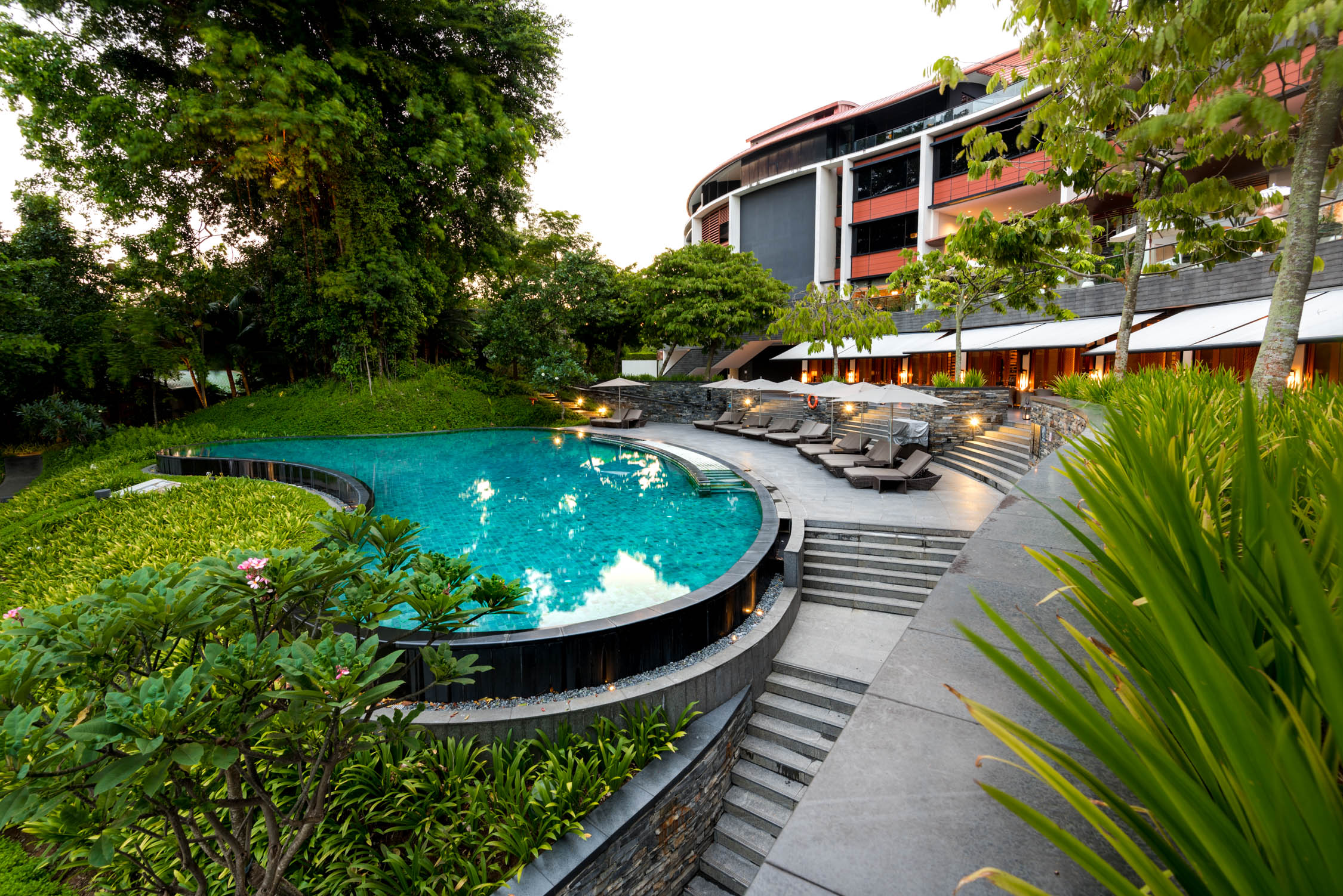 A circular outdoor swimming pool with turquoise water and stone steps surrounded by lush green tropical foliage.