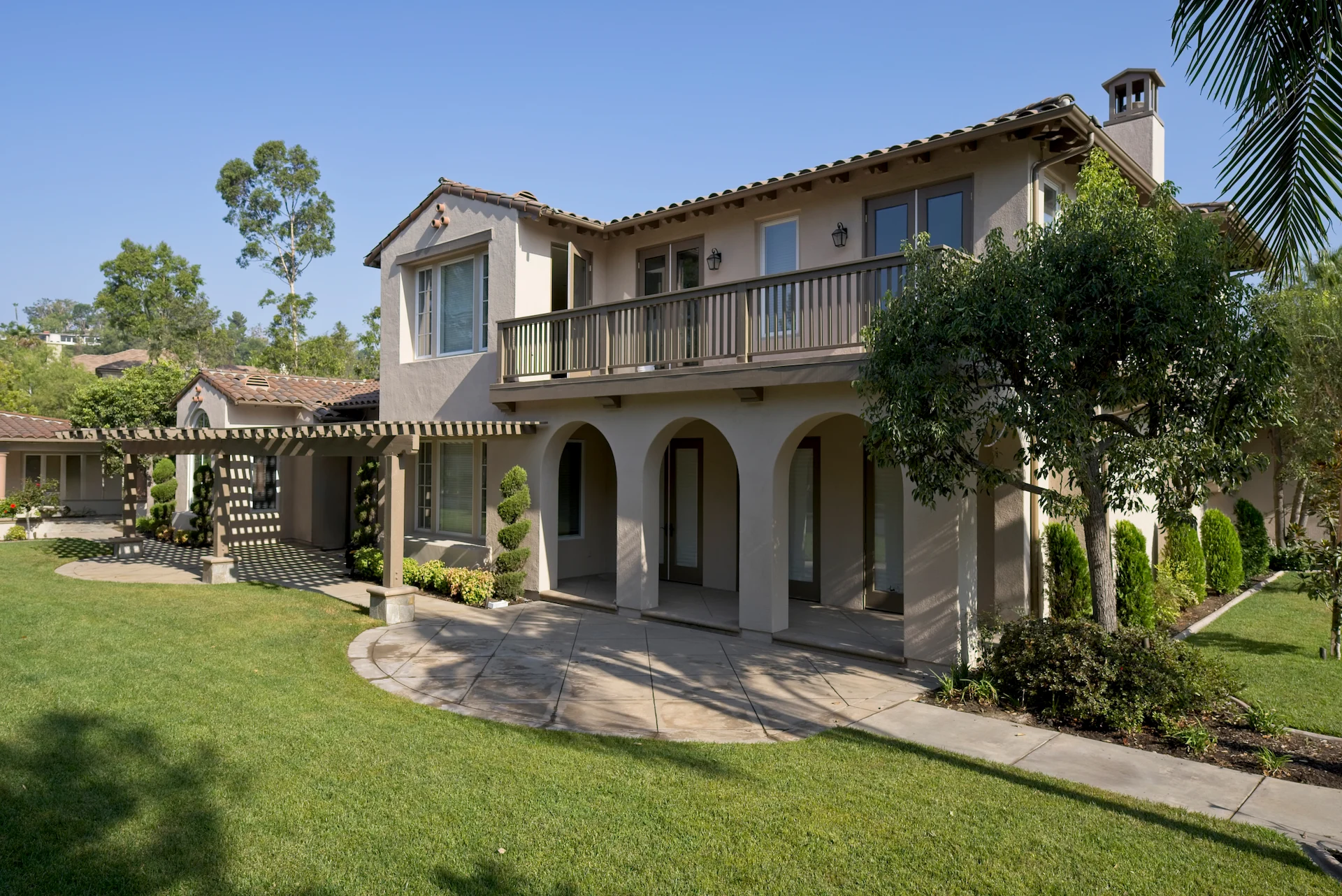 View of the house exterior from the backyard, showcasing the two-story structure with a bedroom balcony, beautifully integrating into the Tustin Ranch Estates' serene outdoor setting. Photo by Todd Huge.
