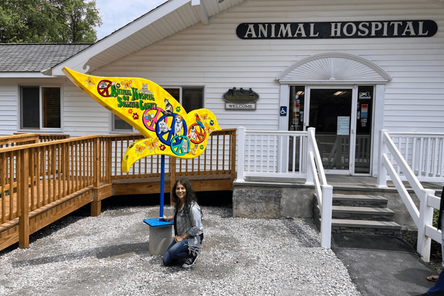 Animal hospital exterior with colorful pet-themed sculpture and woman kneeling beside it at entrance.