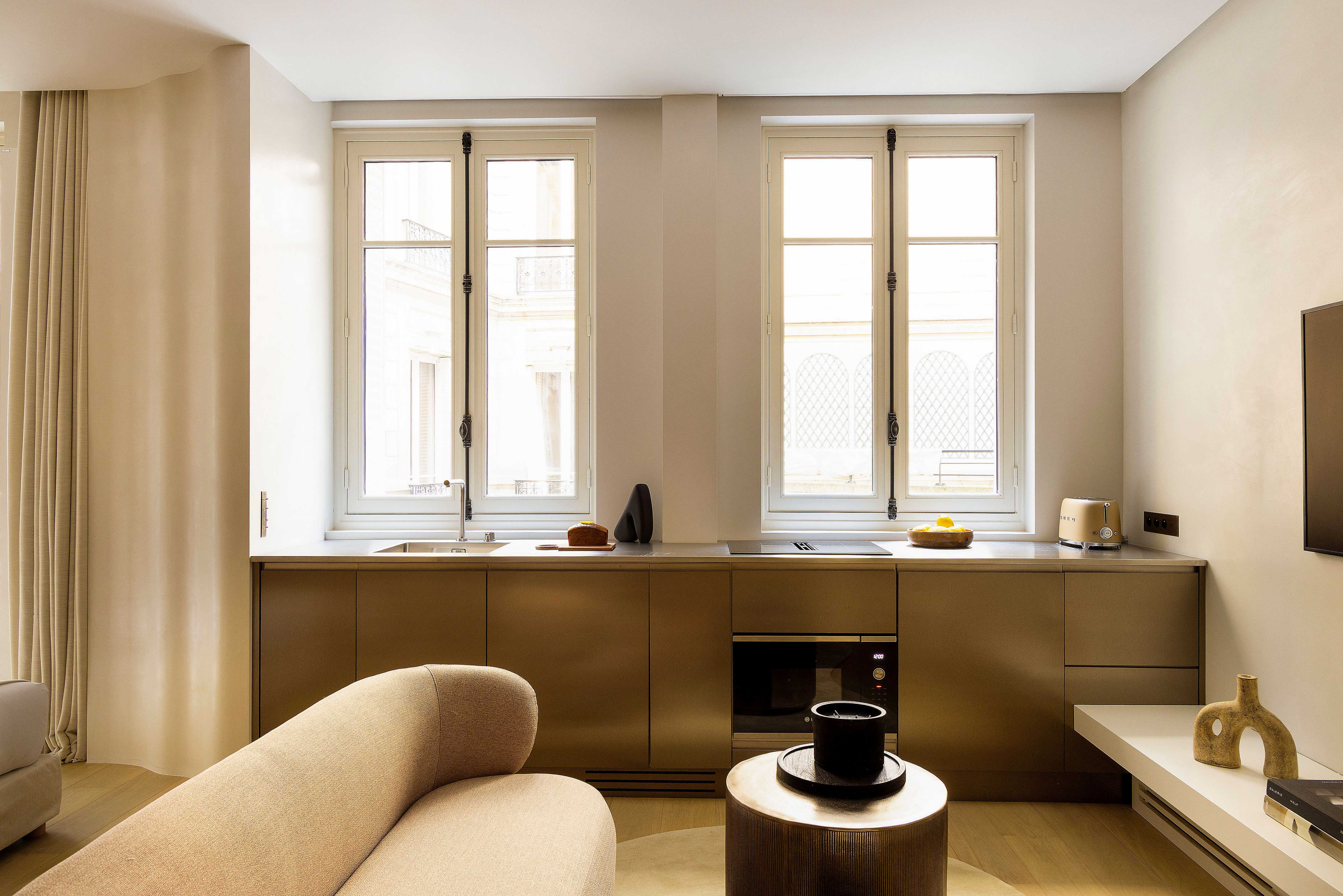 Kitchenette en finition bronze avec canapé beige, vue sur facades parisiennes par les fenetres