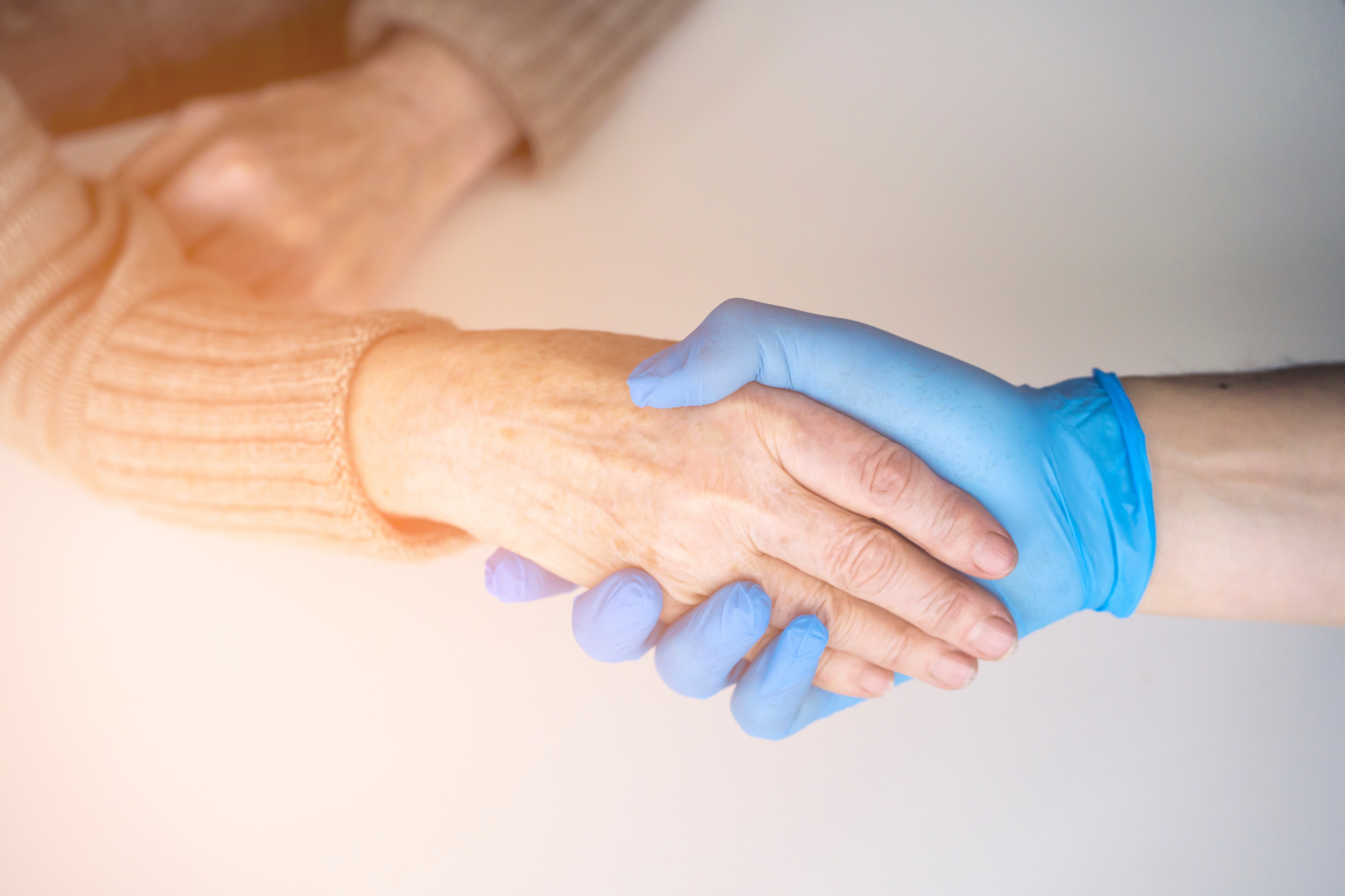 Pflegende Hand mit Handschuh umfasst ältere Hand Quelle Zhanna_AdobeStock