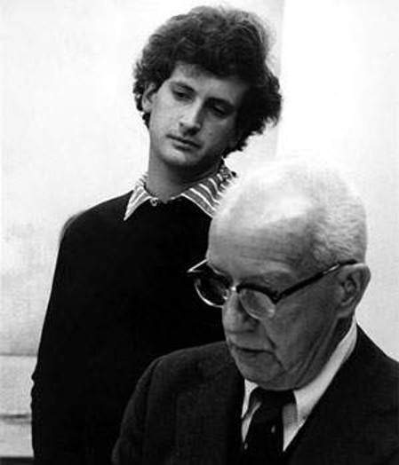 A black and white photo of an old an a young man looking at something.