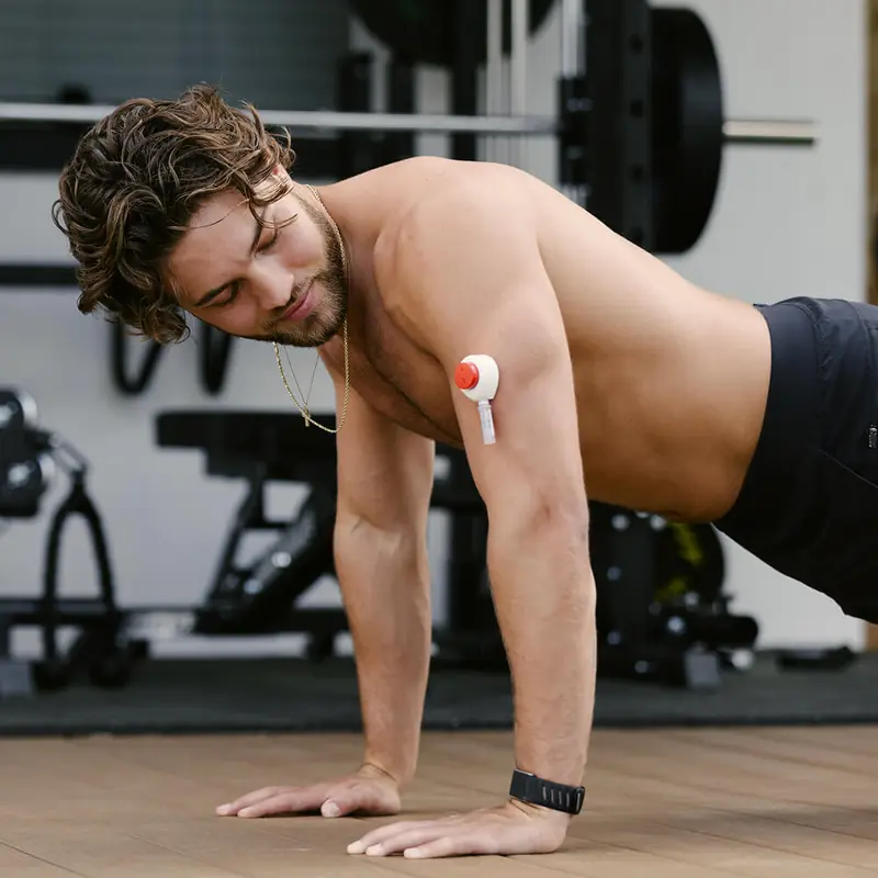 Fit man performing a push-up in a gym environment, with a Rythm Health sensor attached to his upper arm.