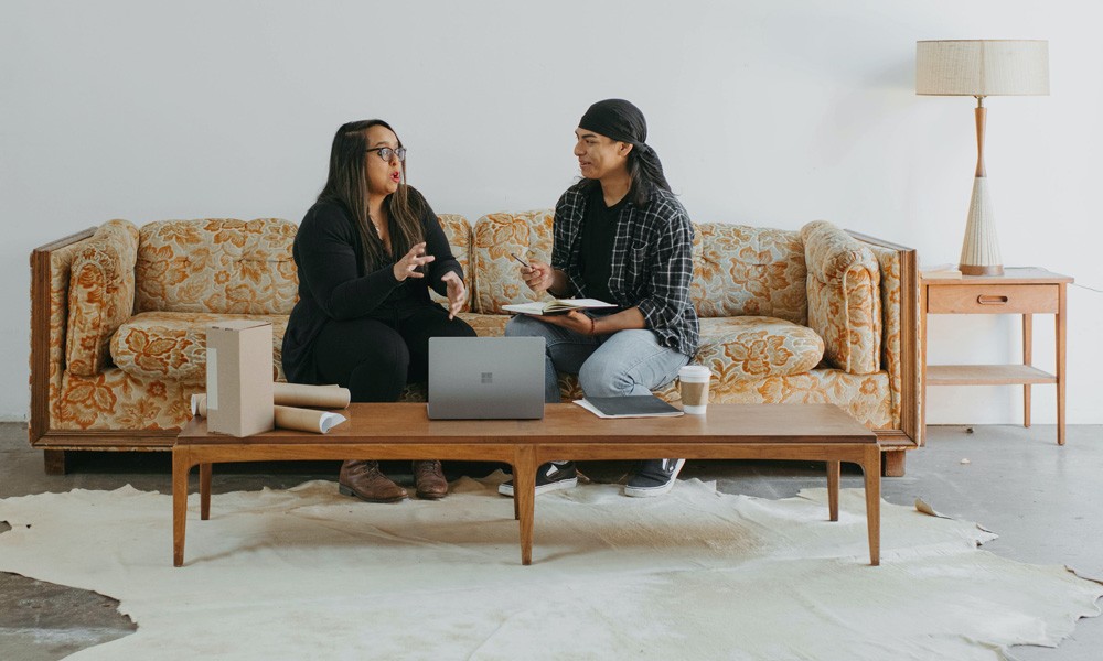 Two colleagues sitting on a sofa having a meeting a front of a laptop. 