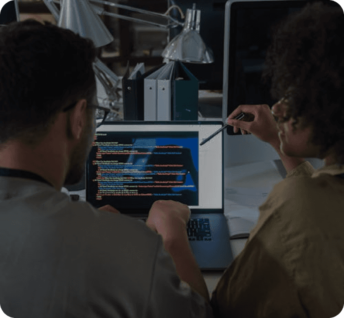 two persons looking at a laptop being used for coding