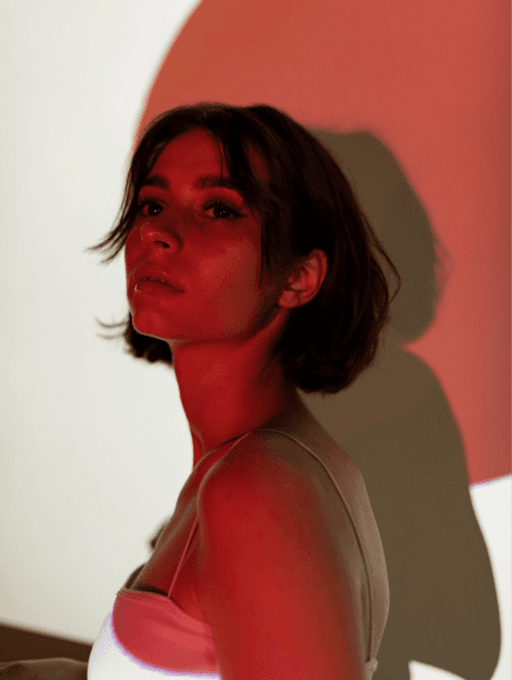 A woman wearing a white top is illuminated by a soft red light, creating a striking visual contrast.