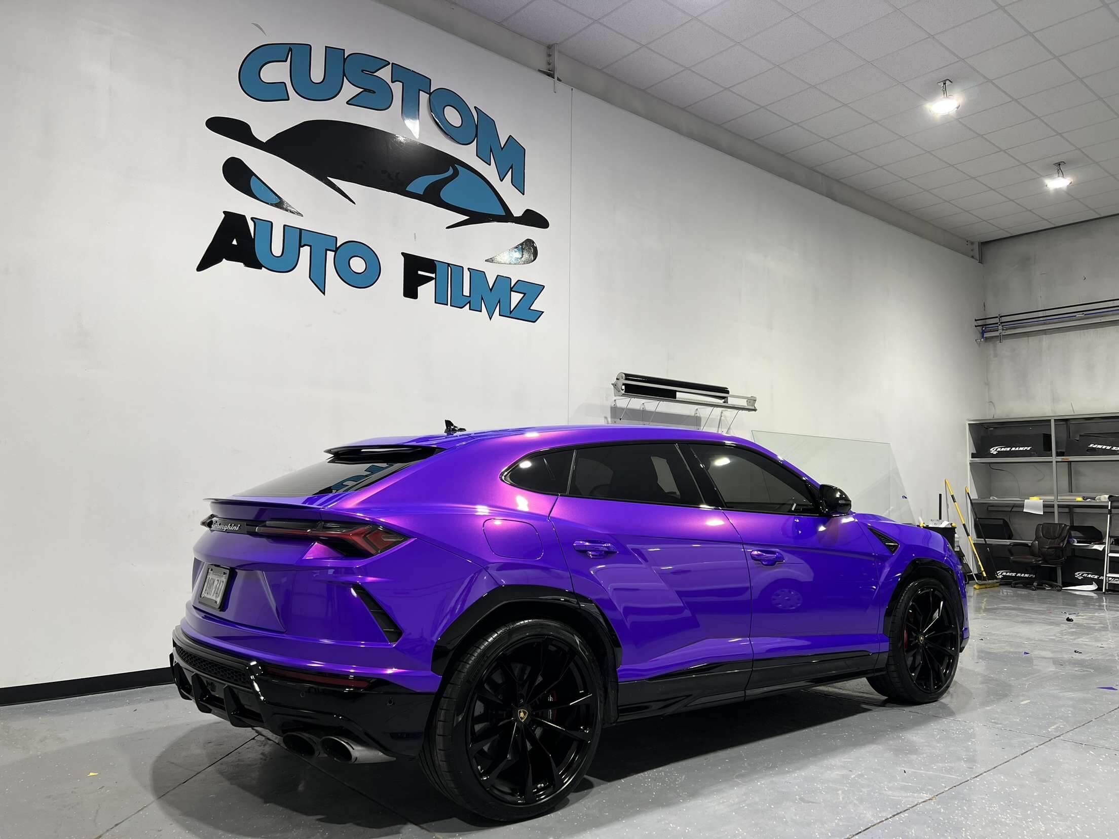 A vibrant purple Lamborghini Urus SUV is parked indoors on a polished gray floor.