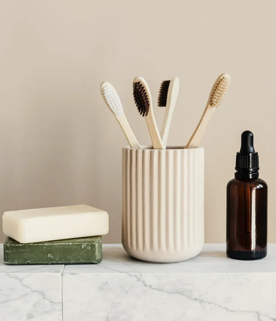 Bamboo toothbrushes in a ribbed ceramic cup on a marble shelf, in soft daylight