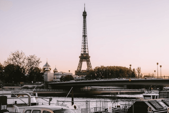 View of the Eiffel Tower at sunset, seen from the Seine with soft pastel skies.