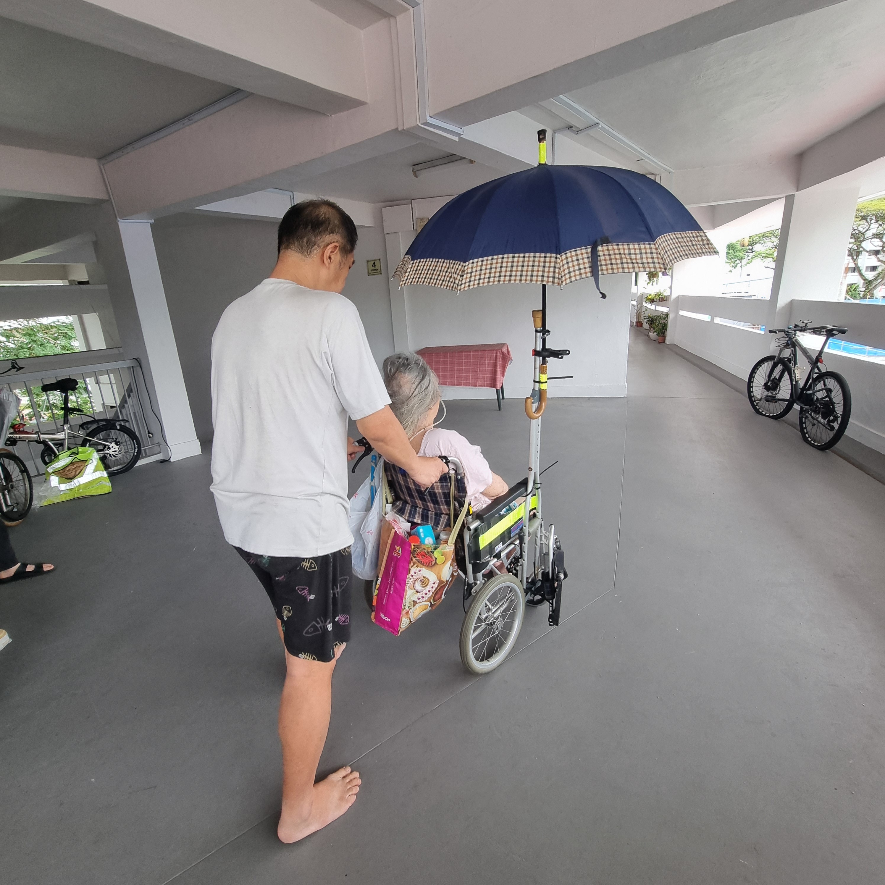 A man pushing the wheelchair of a woman with an umbrella strapped to it