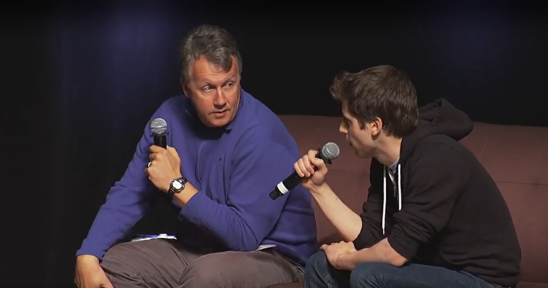 a man with his arms crossed standing in front of a desk