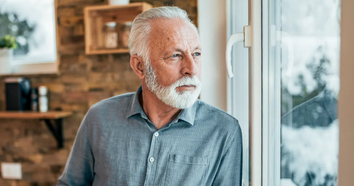 Bilde av en voksen mann som ser ut av vinduet om vinteren.