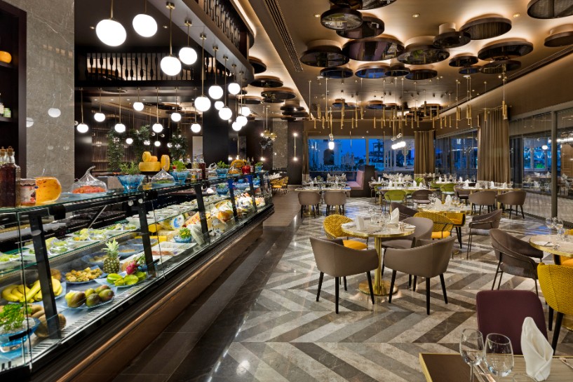 A sophisticated lounge terrace with curved white stucco walls, stone seating, and arched cutouts perfectly framing an unobstructed ocean sunset.