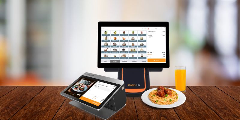 StoreHub POS di atas kaunter dengan pasta dan jus di sebuah kafe.