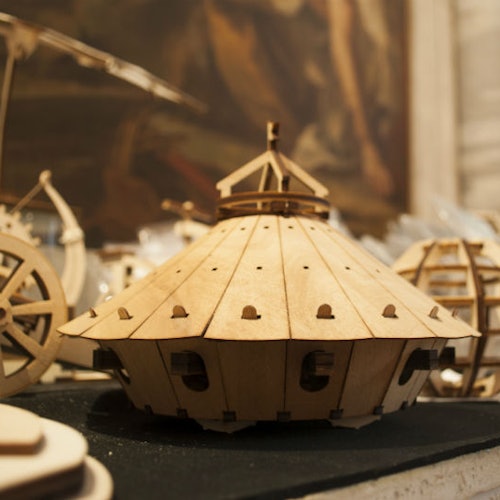 工作坊环境中,一个带有小镂空的穹顶造型木制模型,周围摆放着其他类似的木制模型。